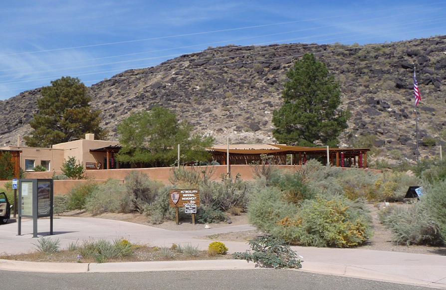 The Petroglyph National Monument visitor center sheltered by stucco walls and canvas canopy at the foot of a rocky hill.