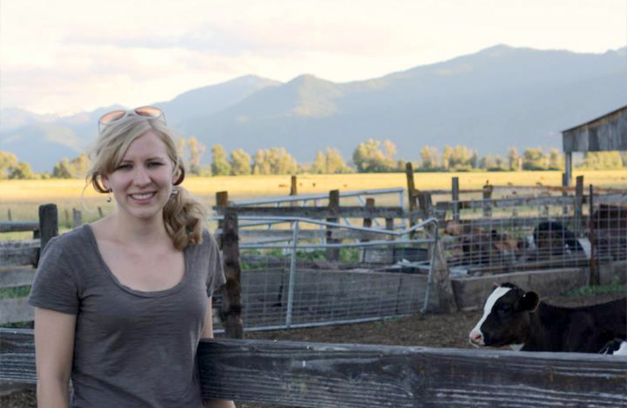 Dr. Nicole Martin smiles next to a fenced in pasture with cows in it and an open field and mountains in the distance