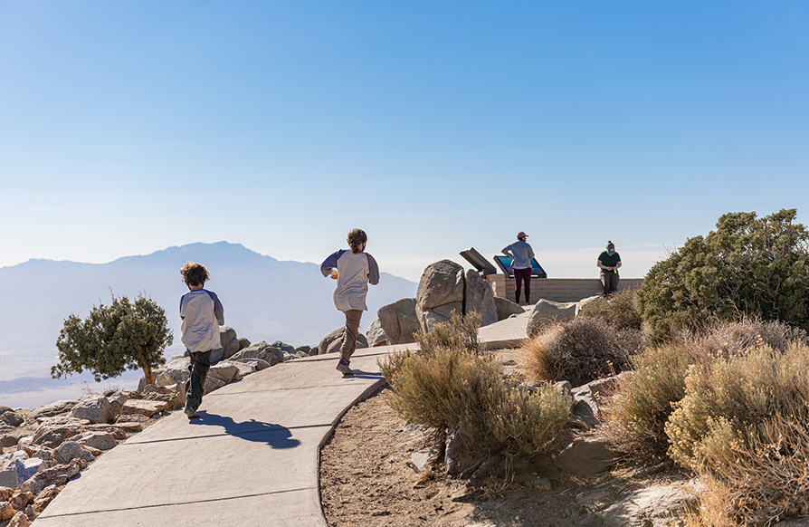 Two kids jog up a paved path to a lookout point in Joshua Tree National Park